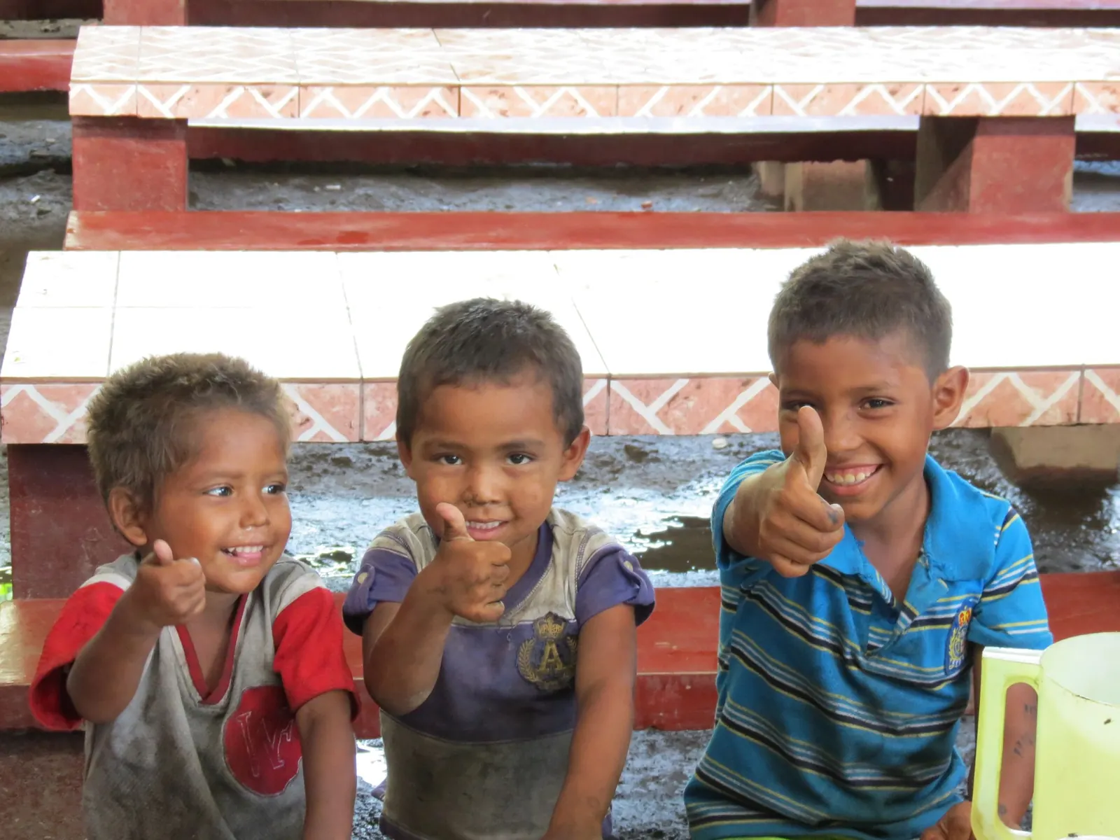 Three children smiling and giving thumbs-up at a ministry program